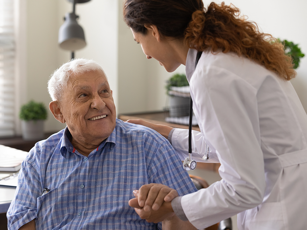 Close up caring nurse holding smiling mature patient hand at meeting in hospital, doctor caregiver w 