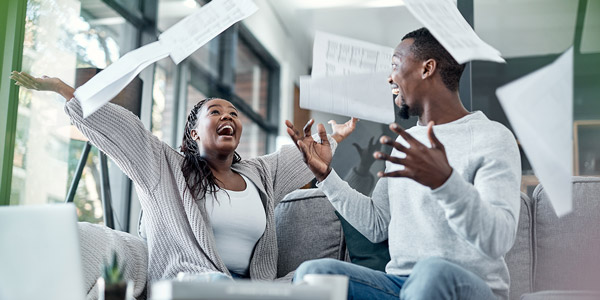 a couple celebrating on the couch with paperwork flying in the air