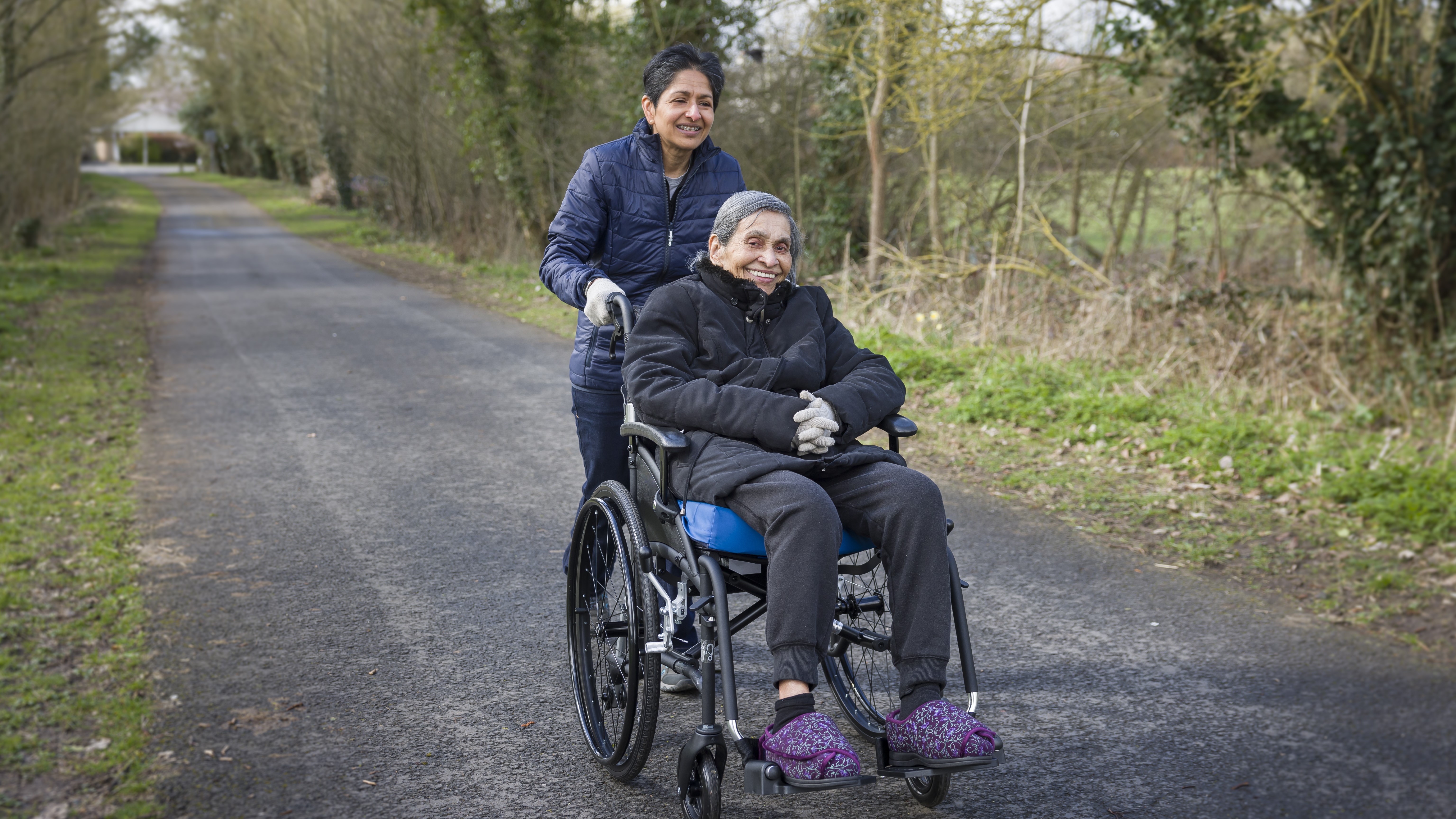 Many in a wheelchair being pushed by a lady in the countryside during winter