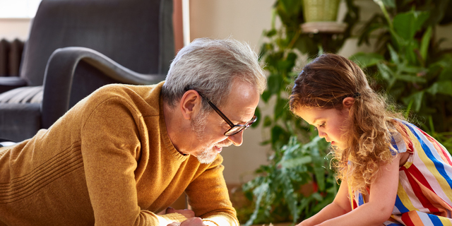 Granddaughter playing with wooden block and granddad watching