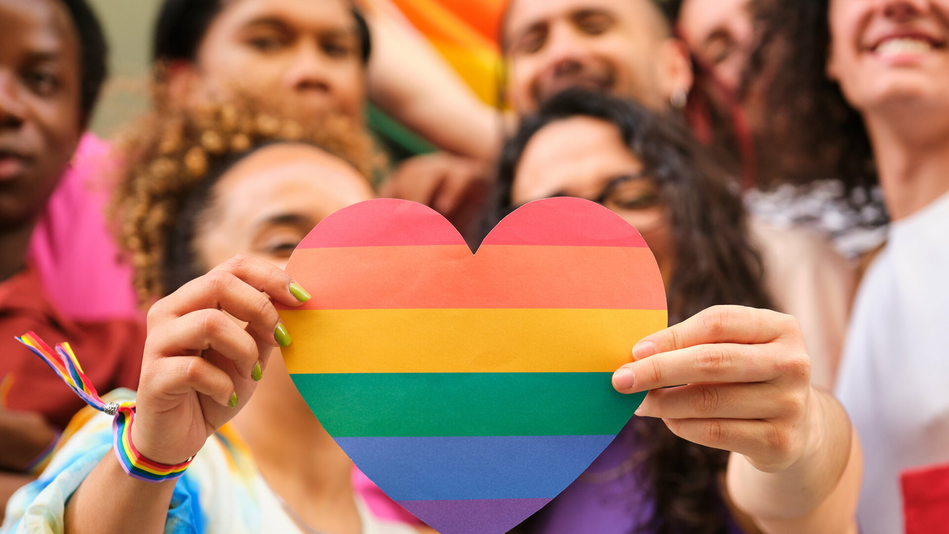 A group of LGBTQ people holding a rainbow heart celebrating Pride Month.