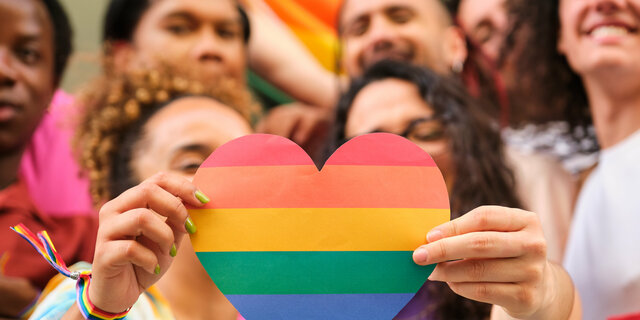 A group of LGBTQ people holding a rainbow heart celebrating Pride Month.