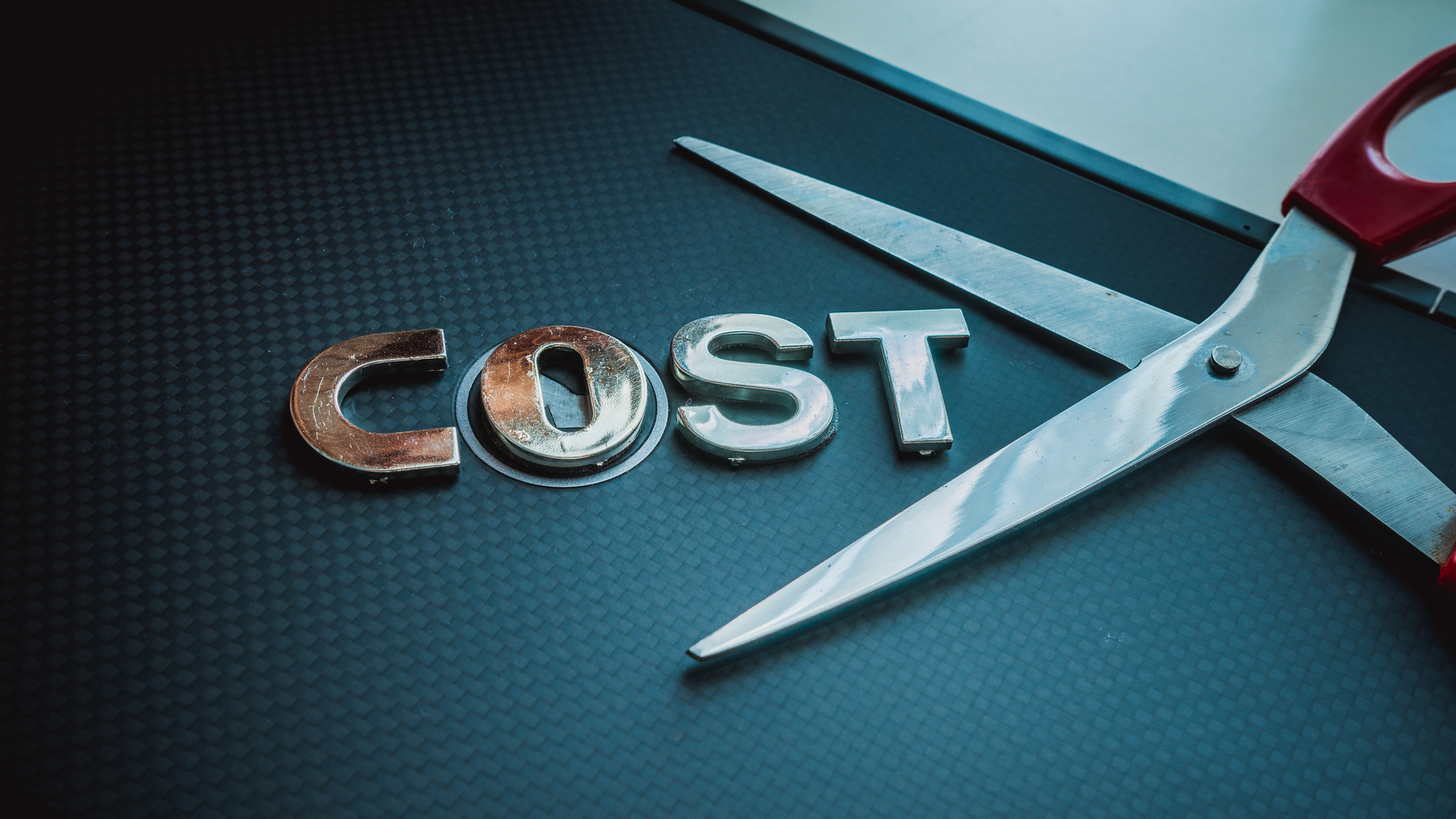 Stainless steel scissor next to word cost. Concept of cost-cutting