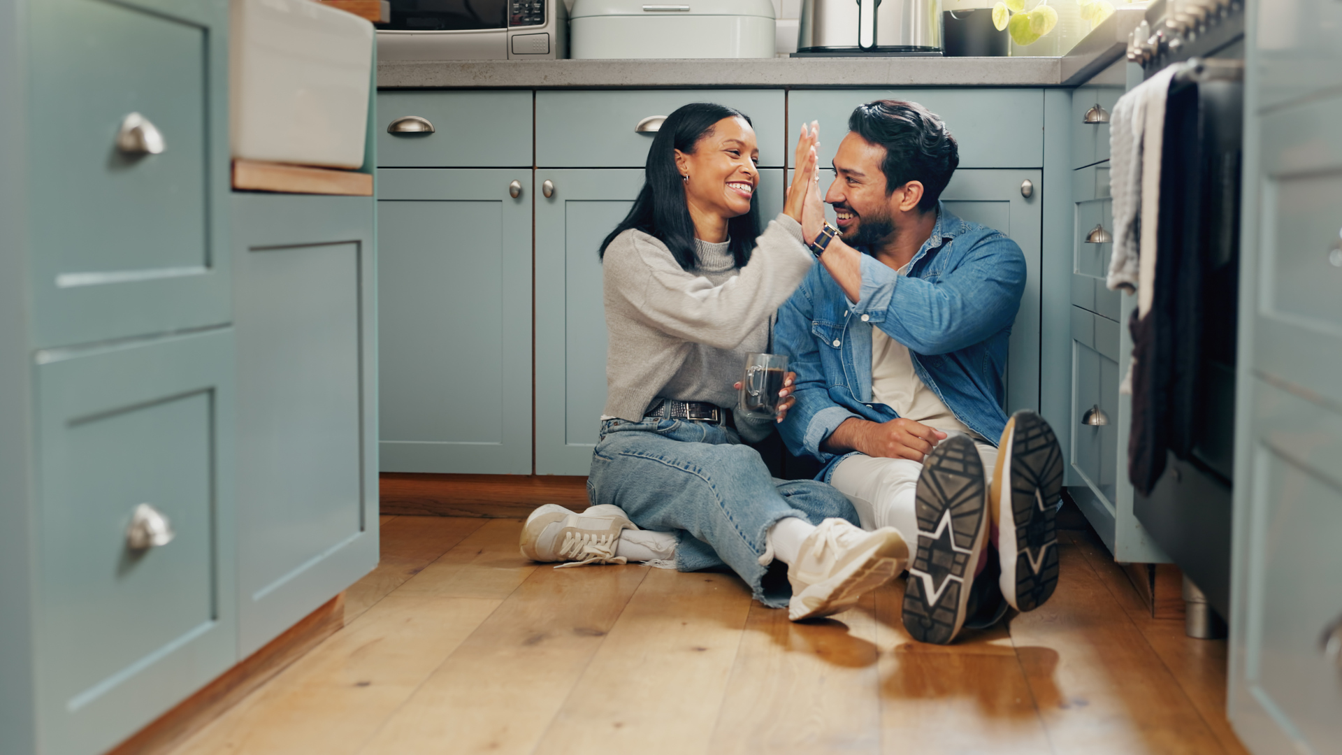 Couple, coffee and sitting on floor in kitchen for quality time or fun to celebrate or discussion. Love, smile and woman with high five are bonding together with caffeine and conversation or care.