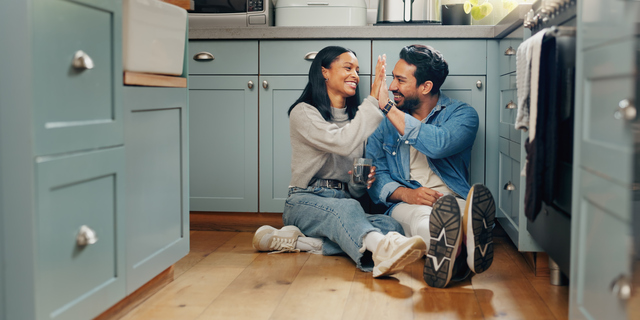 Couple, coffee and sitting on floor in kitchen for quality time or fun to celebrate or discussion. Love, smile and woman with high five are bonding together with caffeine and conversation or care.