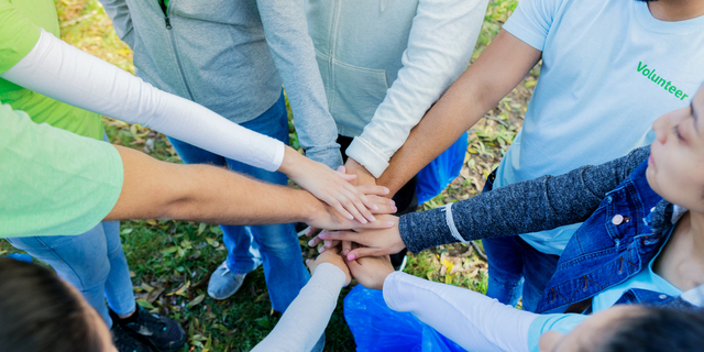 Group of unrecognizable volunteers stack hands before serving