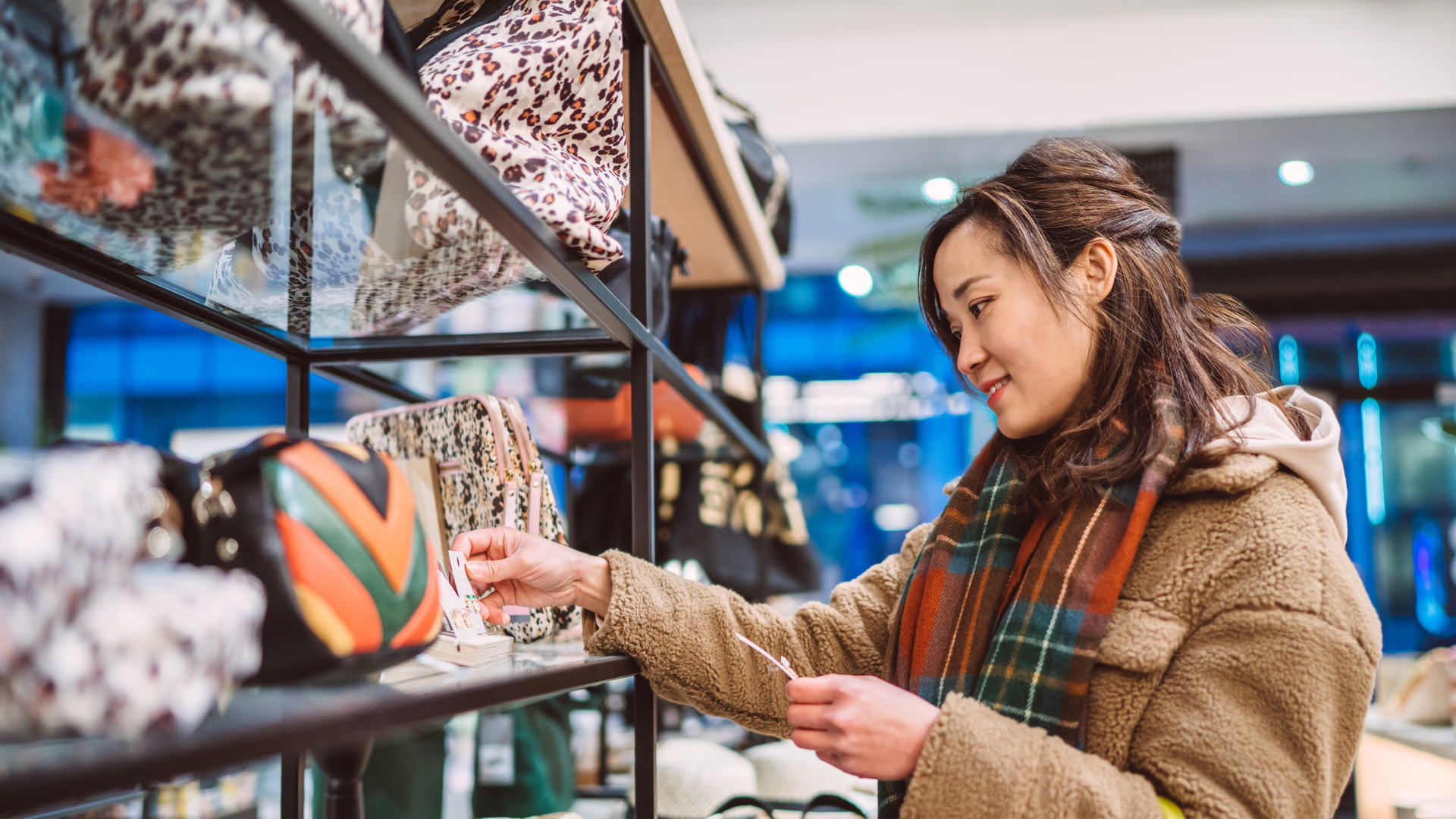 Young cheerful Asian woman shopping for accessories in boutique