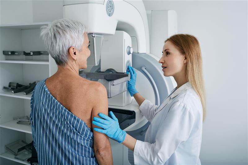 A woman speaking with a doctor during a mammogram.