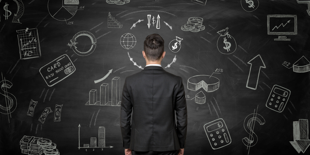 Businessman standing back to us looking at the blackboard with