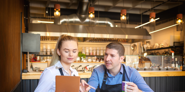 Young man and woman going through paperwork together in their restaurant. Small family restaurant owners discussing finance calculating bills and expenses of their small business.