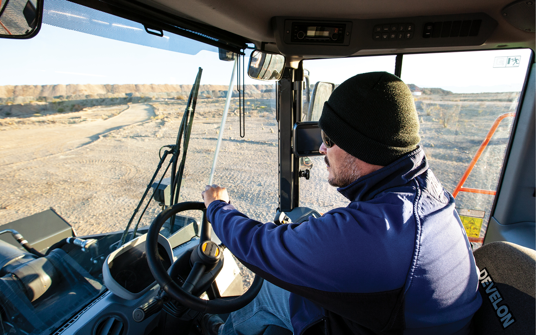 An operator driving a DEVELON wheel loader with large windows for improved visibility.