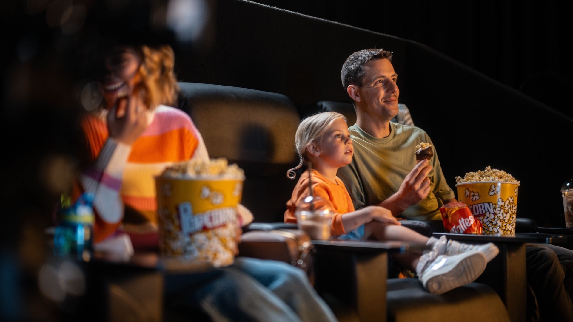 Father and kids watching a movie in cinemas eating popcorn.
