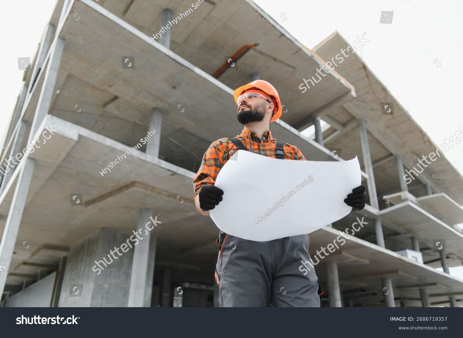 stock-photo-construction-worker-in-hard-hat-and-safety-glasses-holding-blueprint-on-a-concrete-building-2686719357.jpg