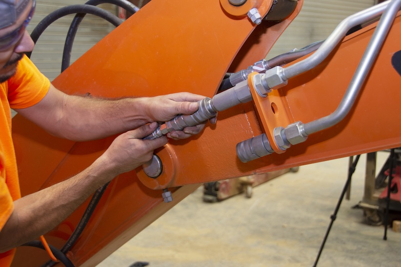 An operator checking a hose on a DEVELON mini excavator.