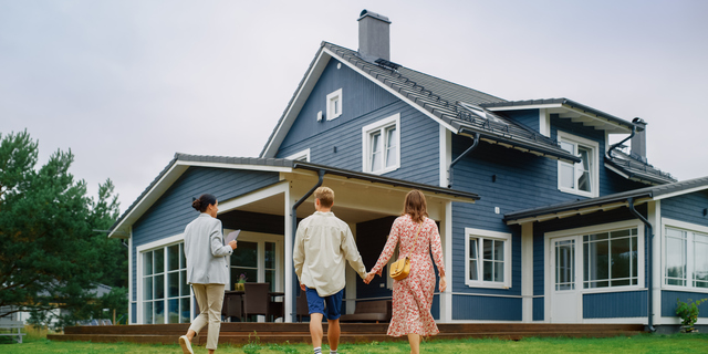 Young Couple Viewing Property for Sale, Talking with Professional Real Estate Agent Outside the House on a Summer Day. Young Beautiful Family are Ready to Become New Homeowners.