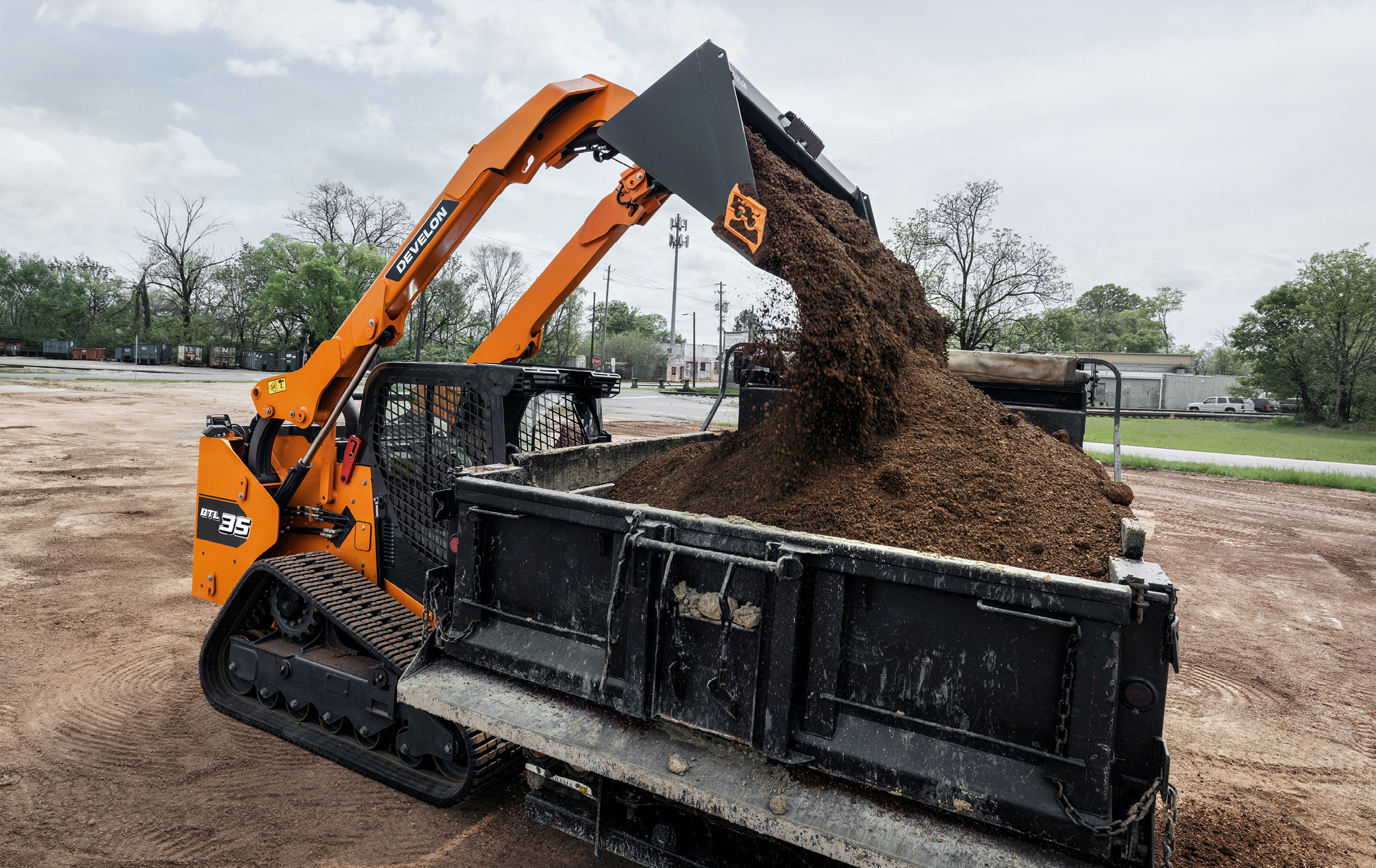 The DEVELON DTL35 compact track loader dumping dirt into a truck bed.