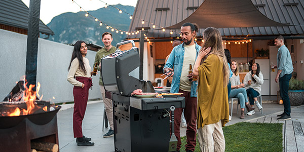 A diverse group of people enjoy a cook-out together in someone's backyard 