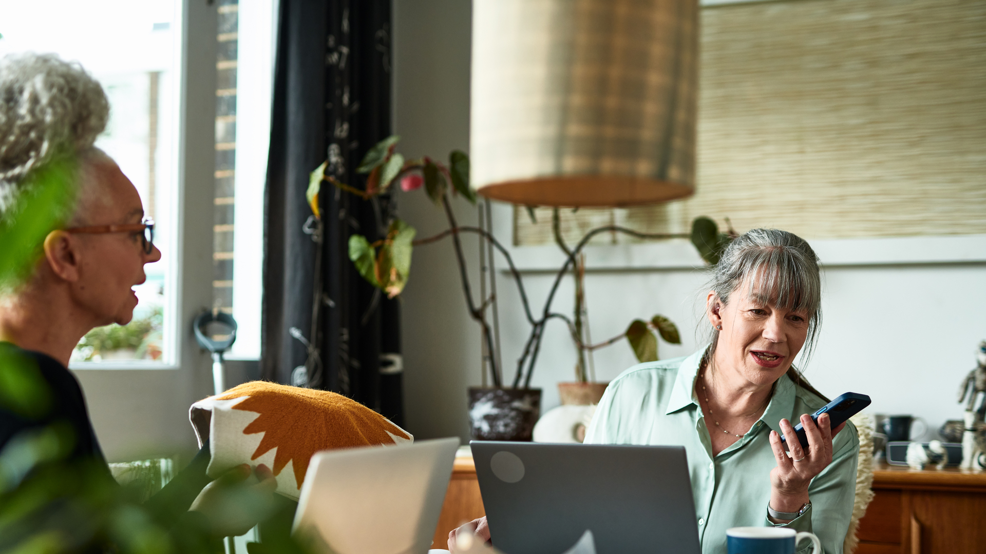 Mature female entrepreneur speaking into smart phone at home