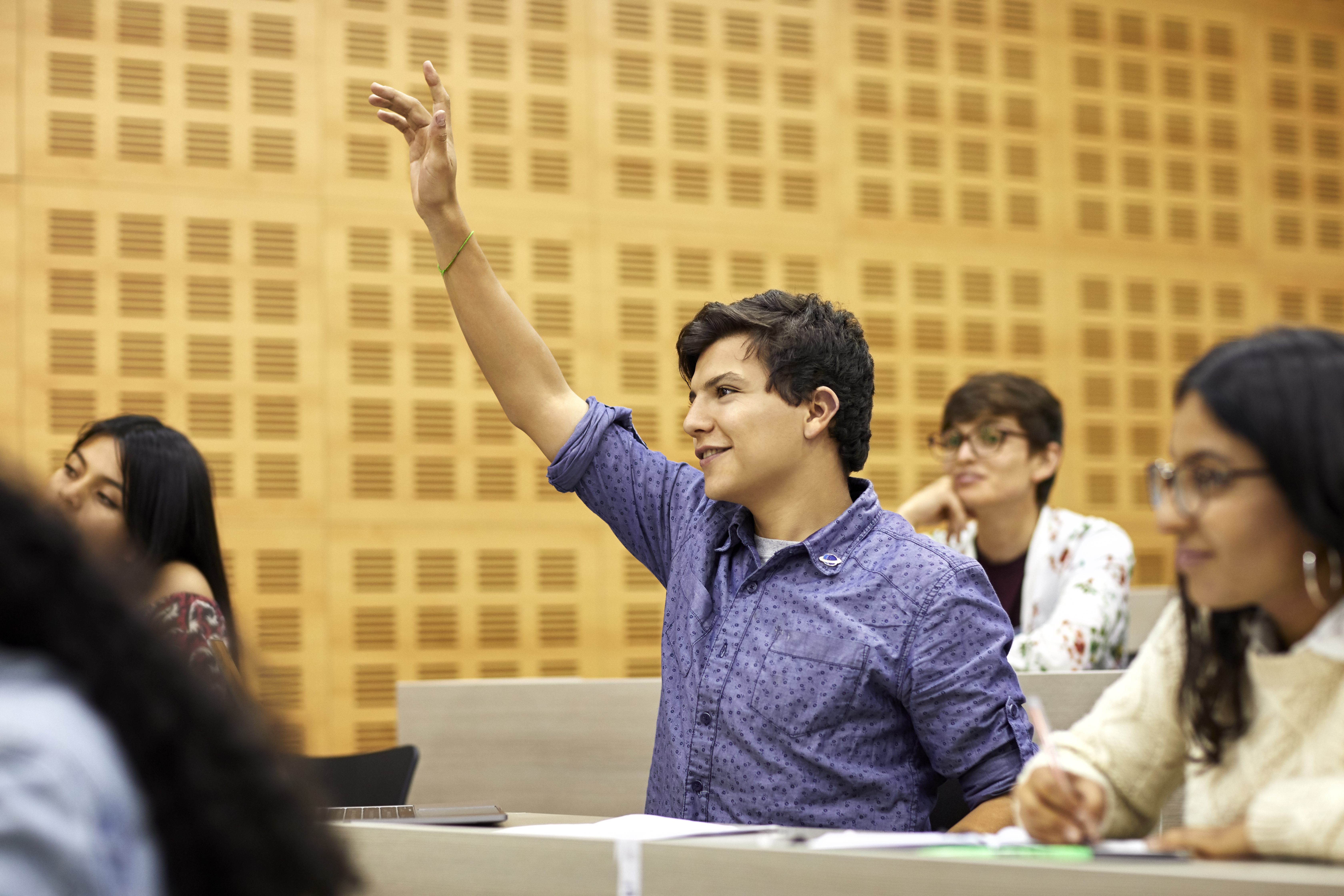 Education technology helps students stay engaged in a classroom, as one student in a purple shirt raises his hand and smiles.