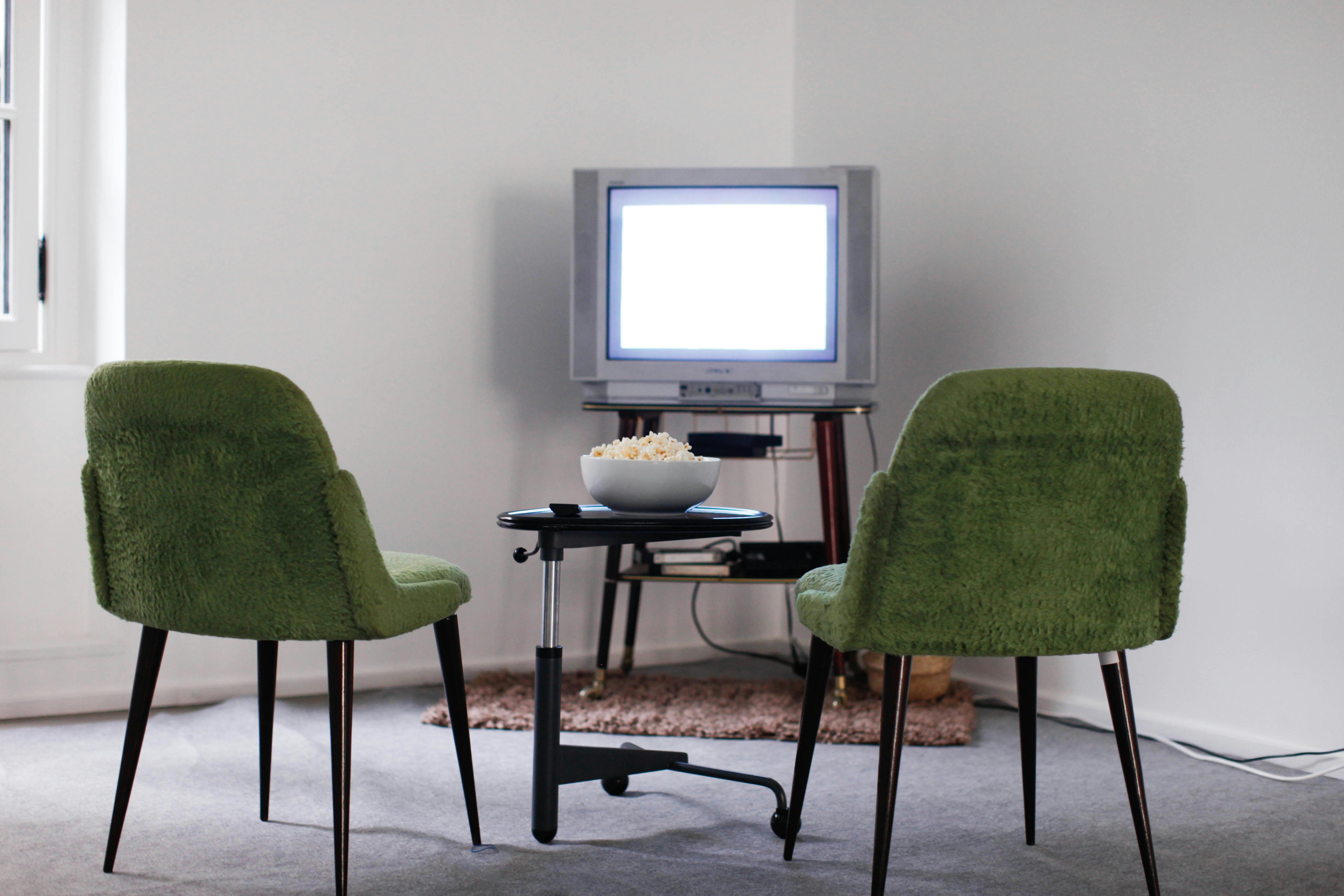 Retro TV setup with green chairs and bowl of popcorn in gallery space
