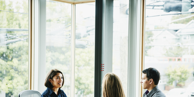 Smiling businesswoman in discussion with clients at office workstation