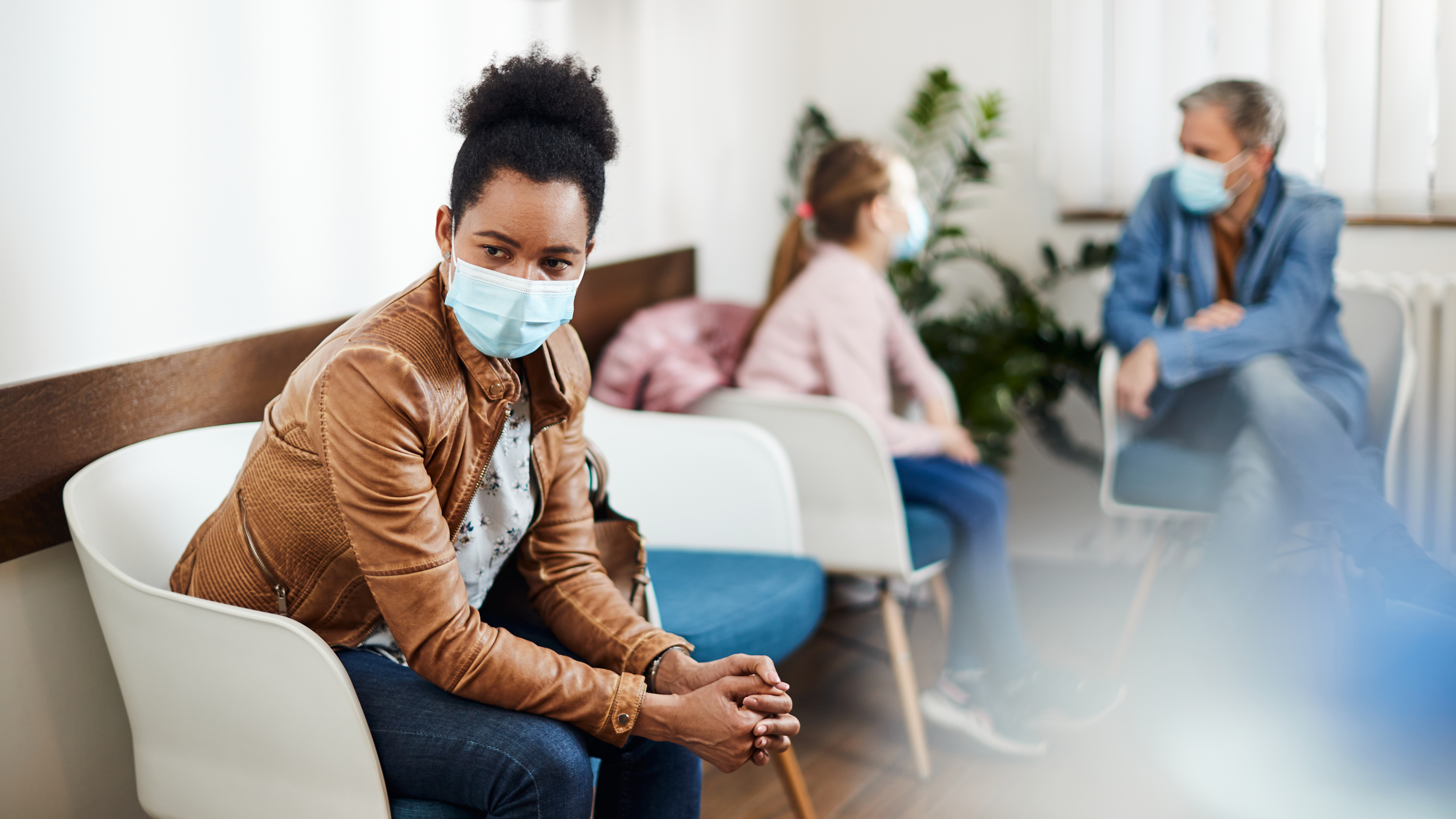 Pensive African American woman wearing protective face mask while waiting for dental appointment at dentist's office.