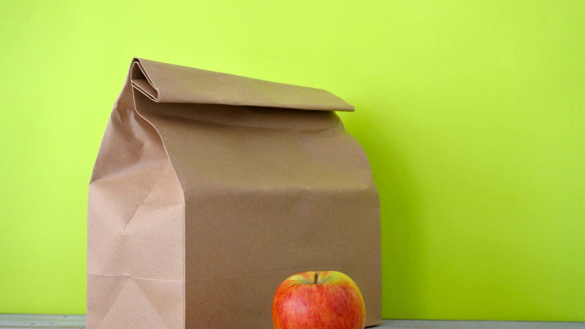 Lunch packed in a brown paper bag with red apple