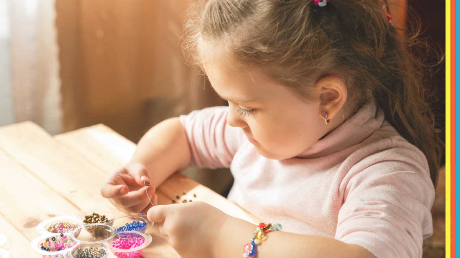 Young child concentrating while creating a bracelet with colourful beads at a craft table, surrounded by bead containers and jewellery-making supplies.