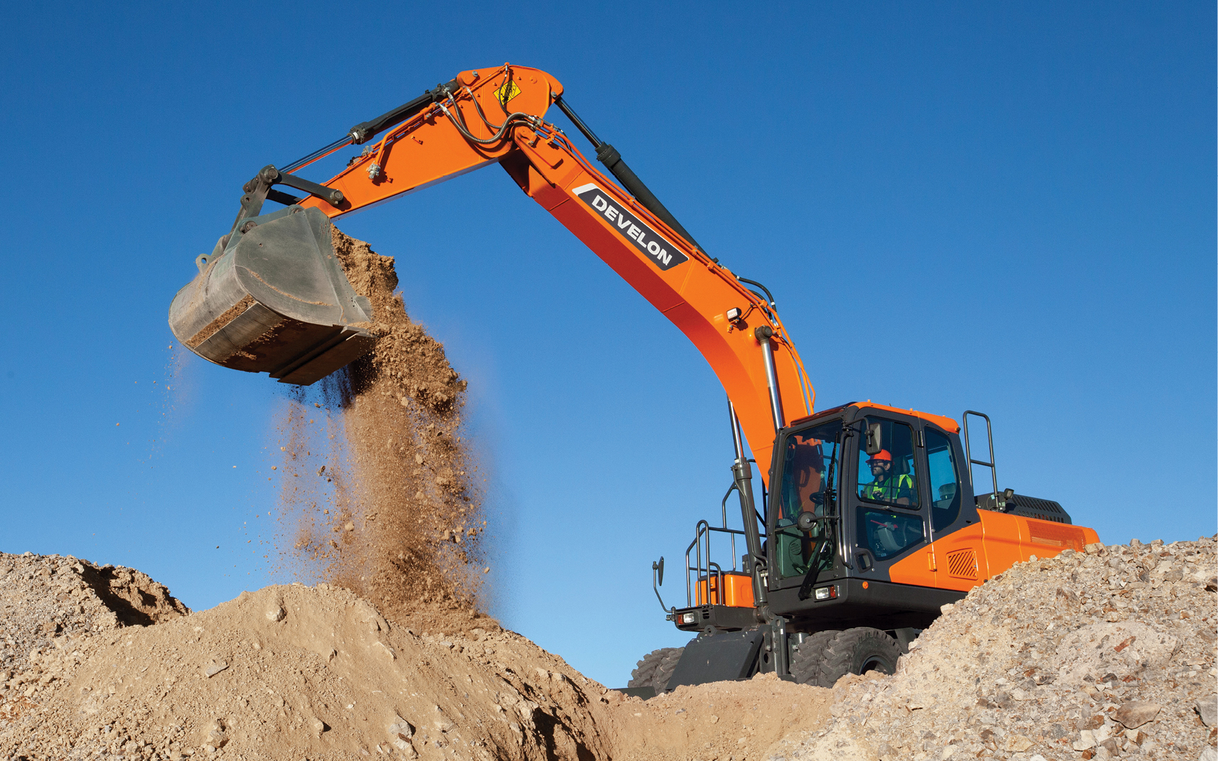 A DEVELON wheel excavator scooping dirt on a job site. 