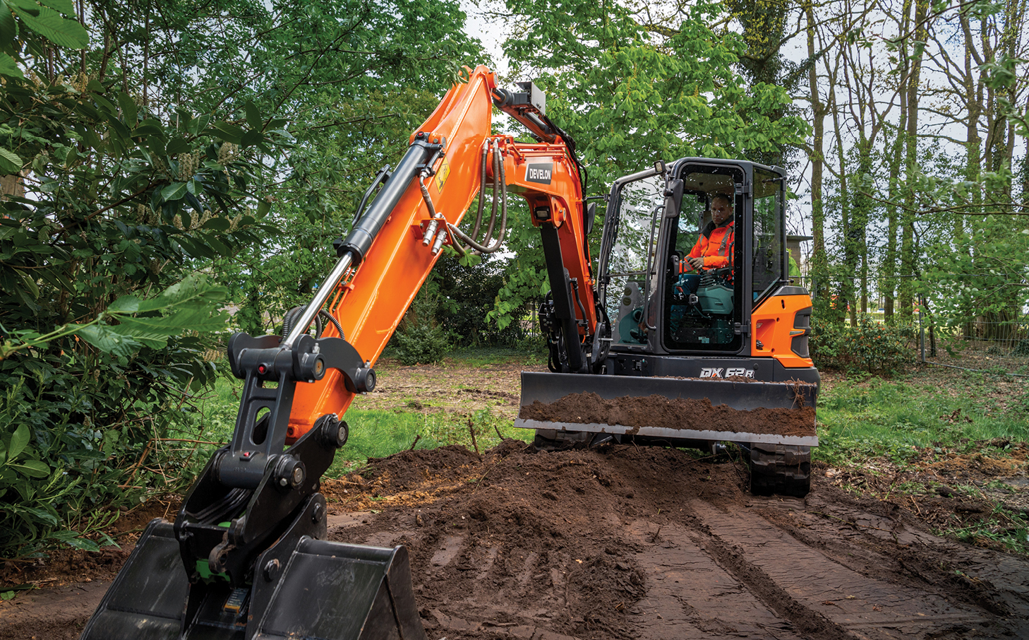 A DEVELON mini excavator with bucket grading dirt on a tree-lined piece of farmland.