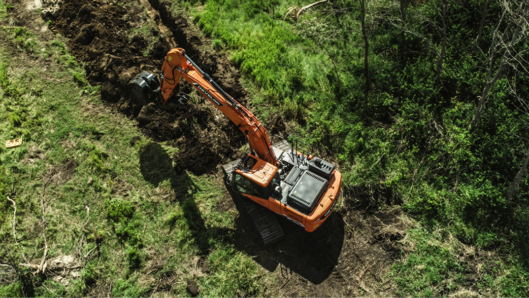 Overhead view of a DEVELON crawler excavator digging a trench on a piece of land.