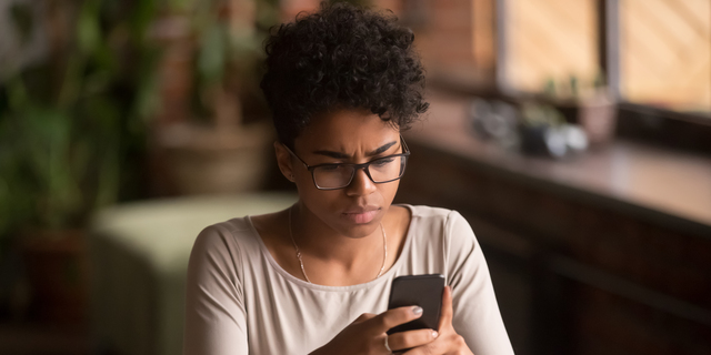 Upset confused african woman holding cellphone having problem with phone