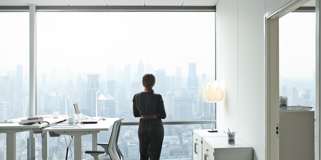 Businesswoman standing inside office and looking out of big window with beautiful view of skyline