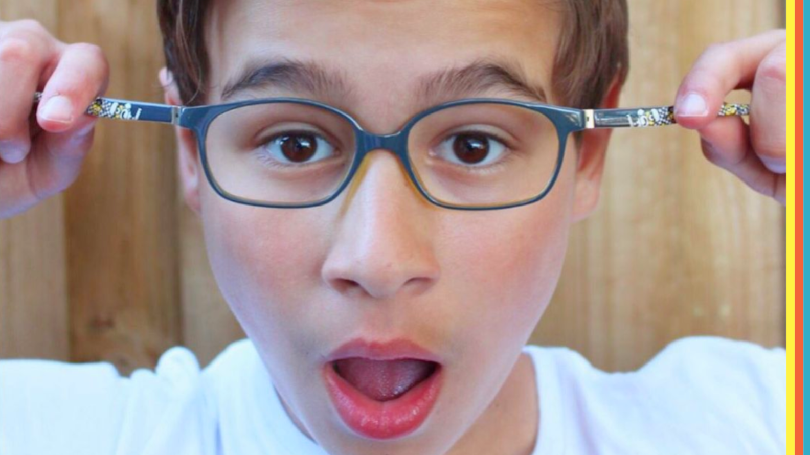 Child wearing blue Minions-themed eyeglasses with a surprised expression, holding the frame arms out to show the Minions design. Colourful striped border on the right side.