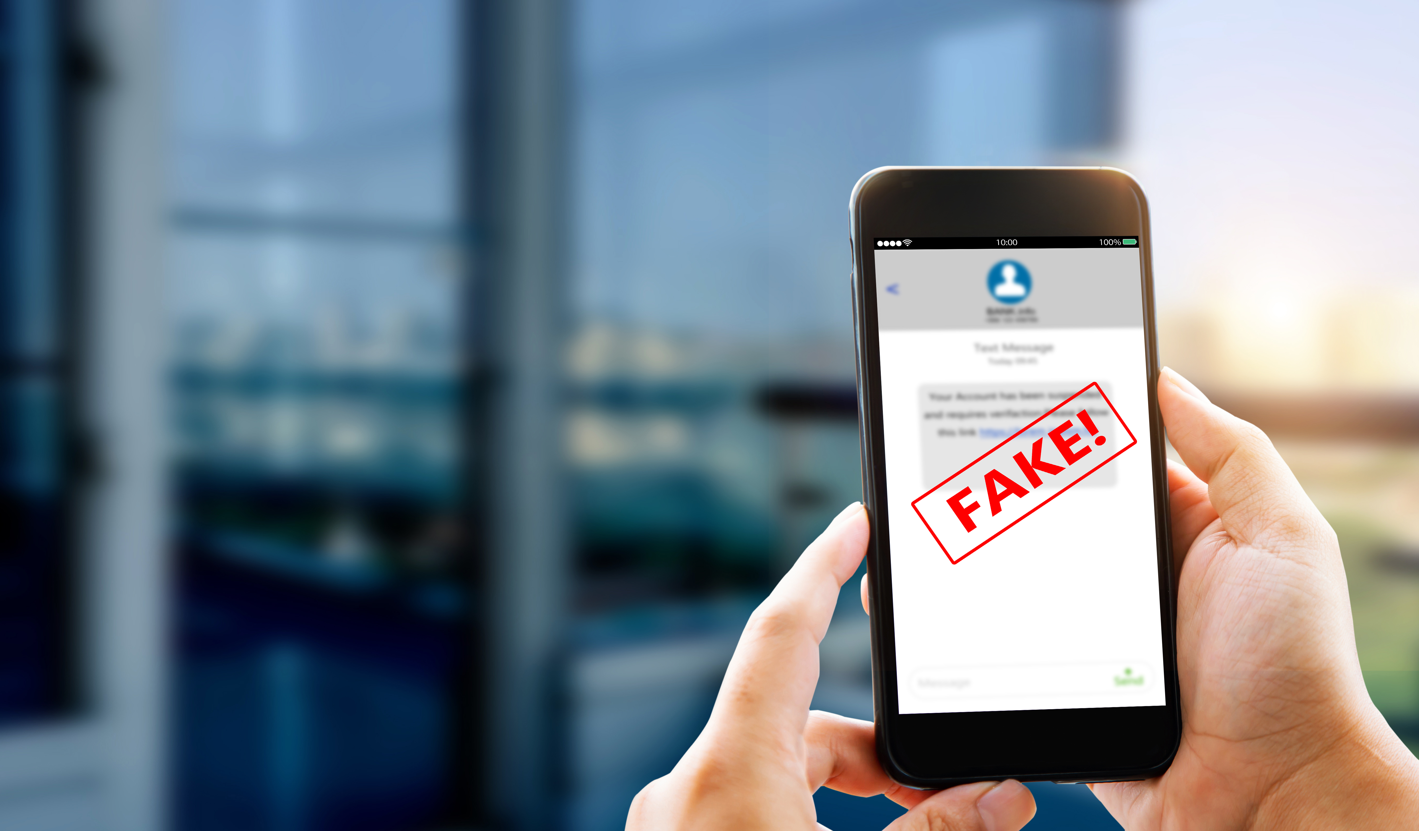Close-up of a person holding a smartphone displaying a text message marked “FAKE!” in red, warning of a phishing or scam message.