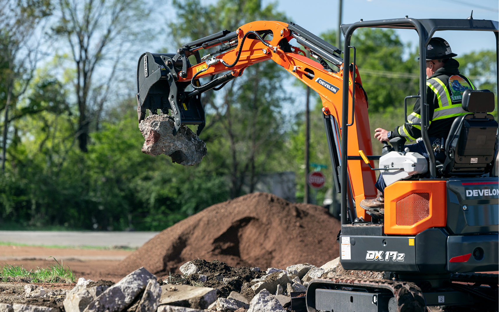 An operator lifts broken concrete with a bucket and thumb.