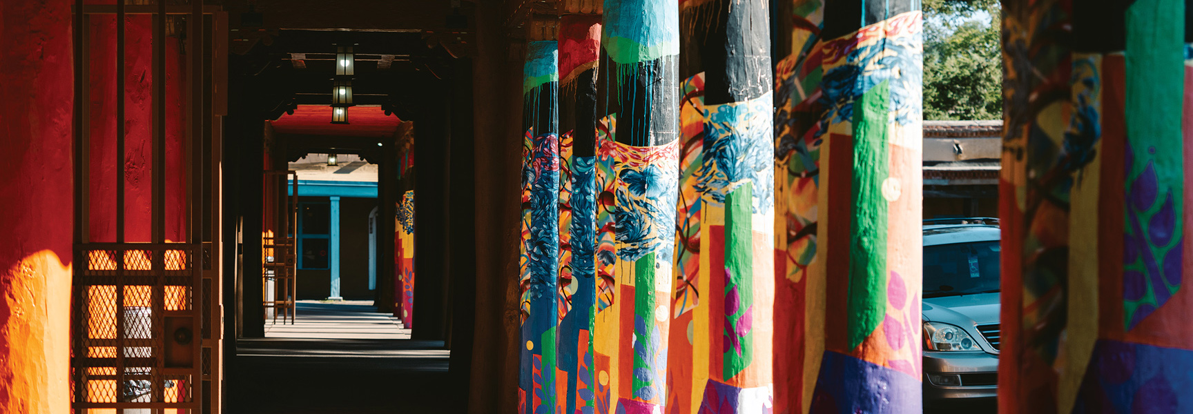 A row of colorfully painted pillars lines a shaded outdoor walkway in New Mexico.