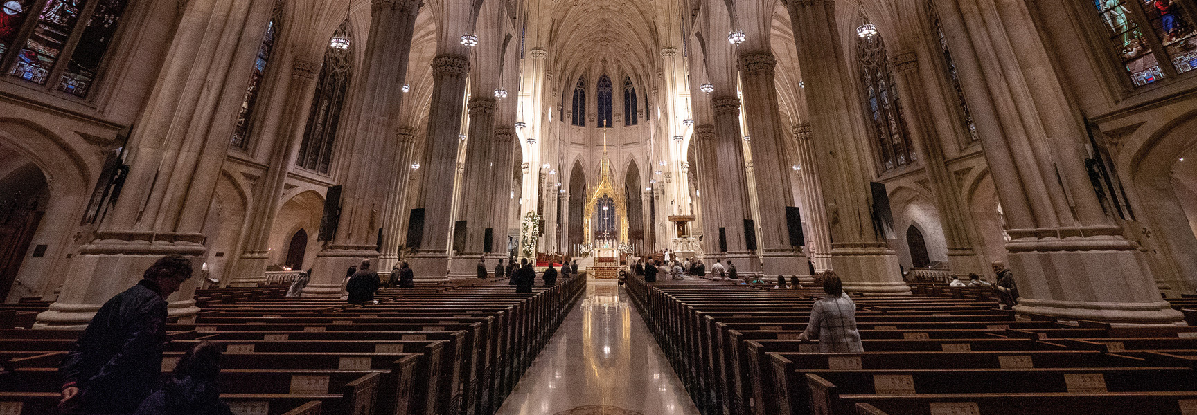 The grand, vaulted interior of a historic cathedral in Georgia, with rows of wooden pews filled with visitors looking towards the altar.