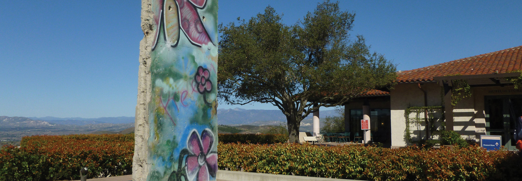 A graffiti-covered section of the Berlin Wall stands outdoors at the Reagan Library, with the rolling hills of California visible in the background.