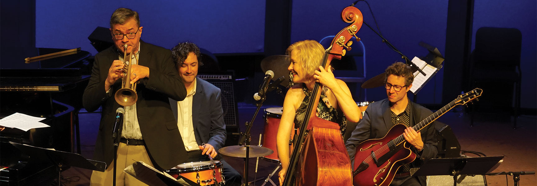 A four-person jazz band performs on stage with a trumpet, drums, upright bass, and guitar at the Oregon Festival of American Music.