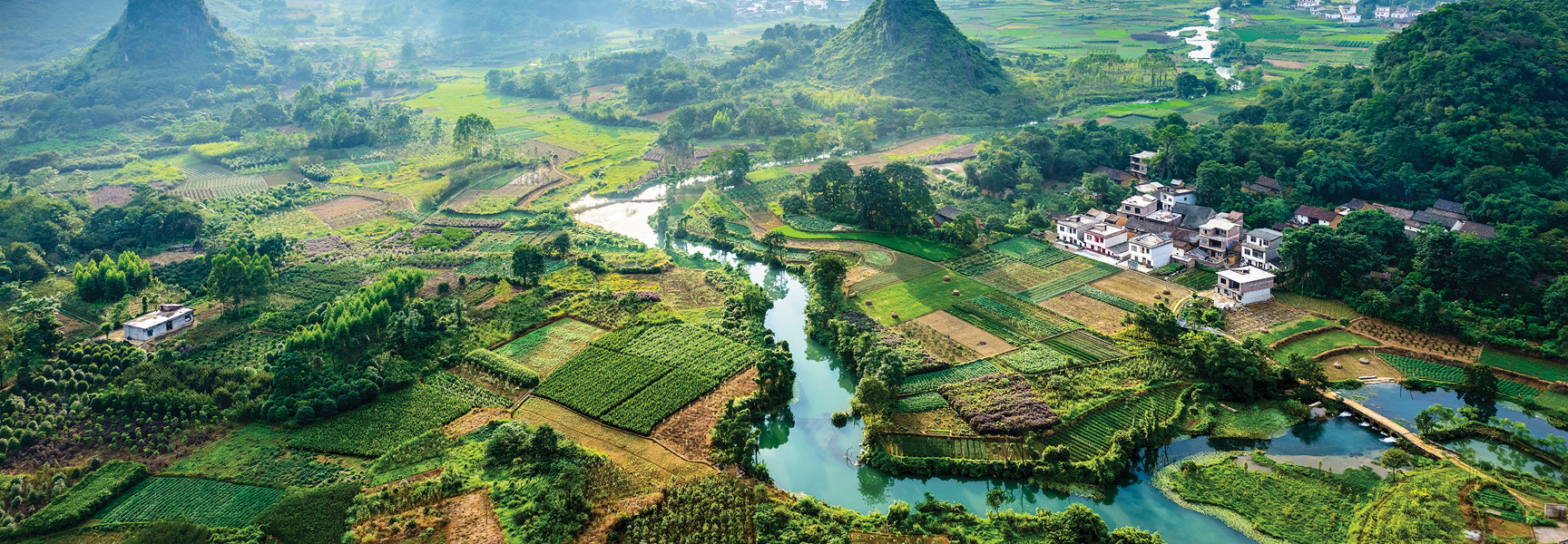 Aerial view of a river winding through a lush valley of green fields and villages in China.