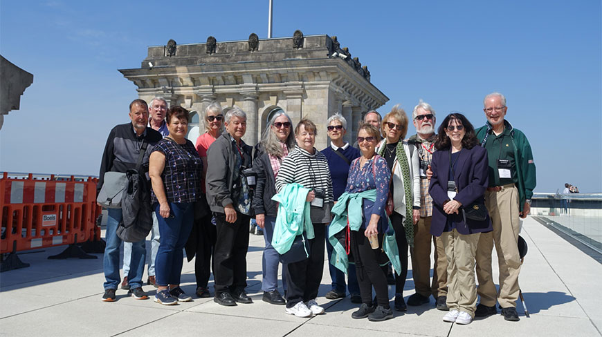 A group of travelers poses for a photo on the rooftop of the Reichstag building in Germany on a sunny day.