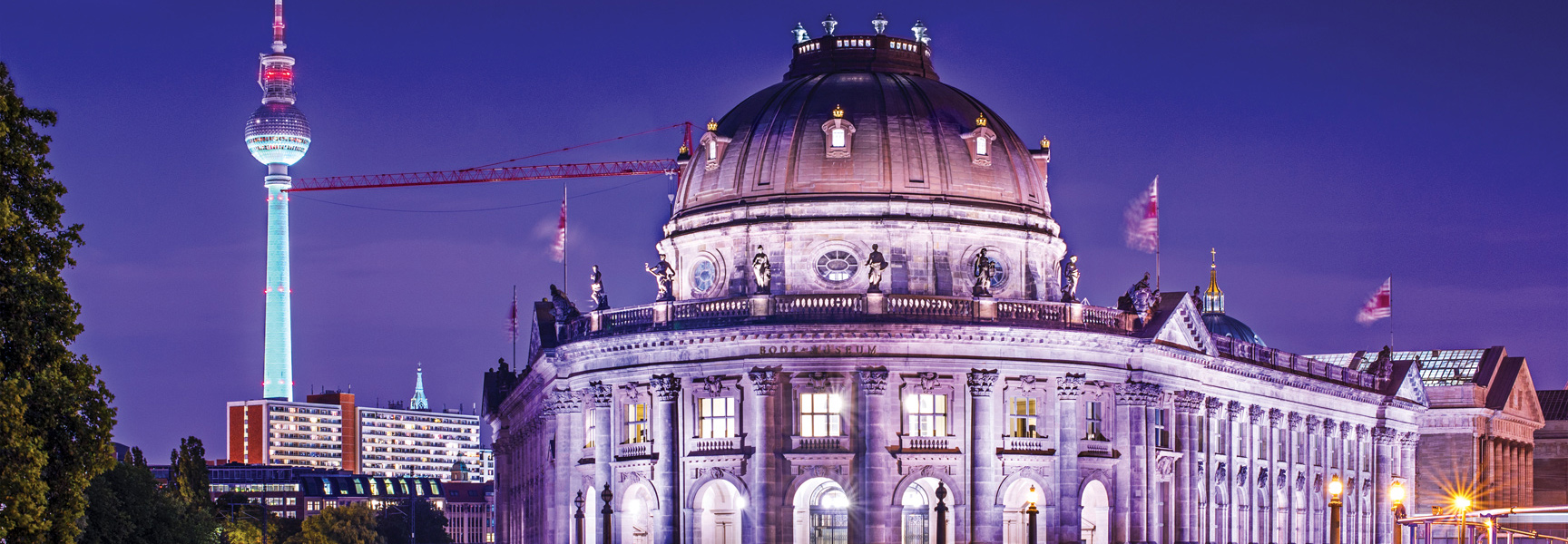 The Bode Museum and the TV Tower are illuminated against a purple night sky in Berlin, Germany.