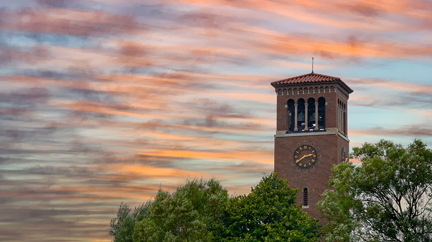 The Chautauqua Bell Tower in New York rises above the treetops against a beautiful, multi-colored sunset.
