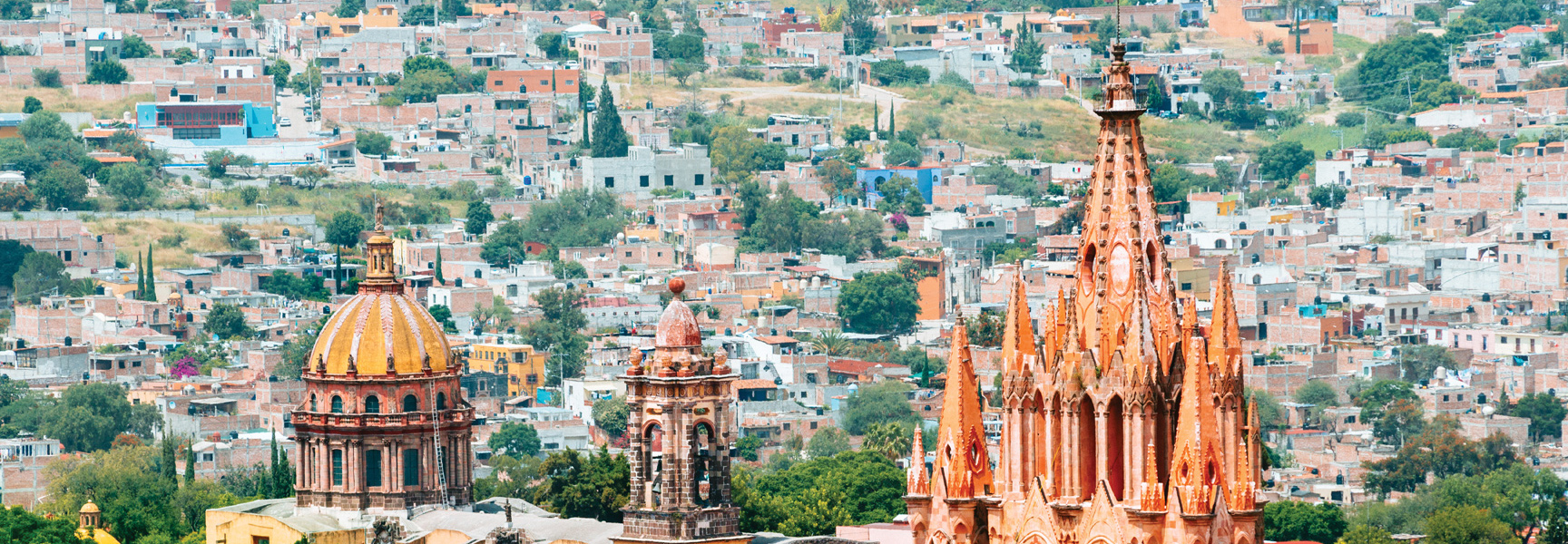 Ornate church spires and a large dome overlook the colorful, densely packed hillside city of San Miguel de Allende, Mexico.