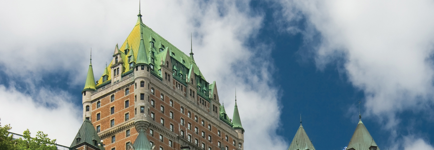 The green-roofed Château Frontenac hotel in Québec City stands tall against a blue sky with white clouds.