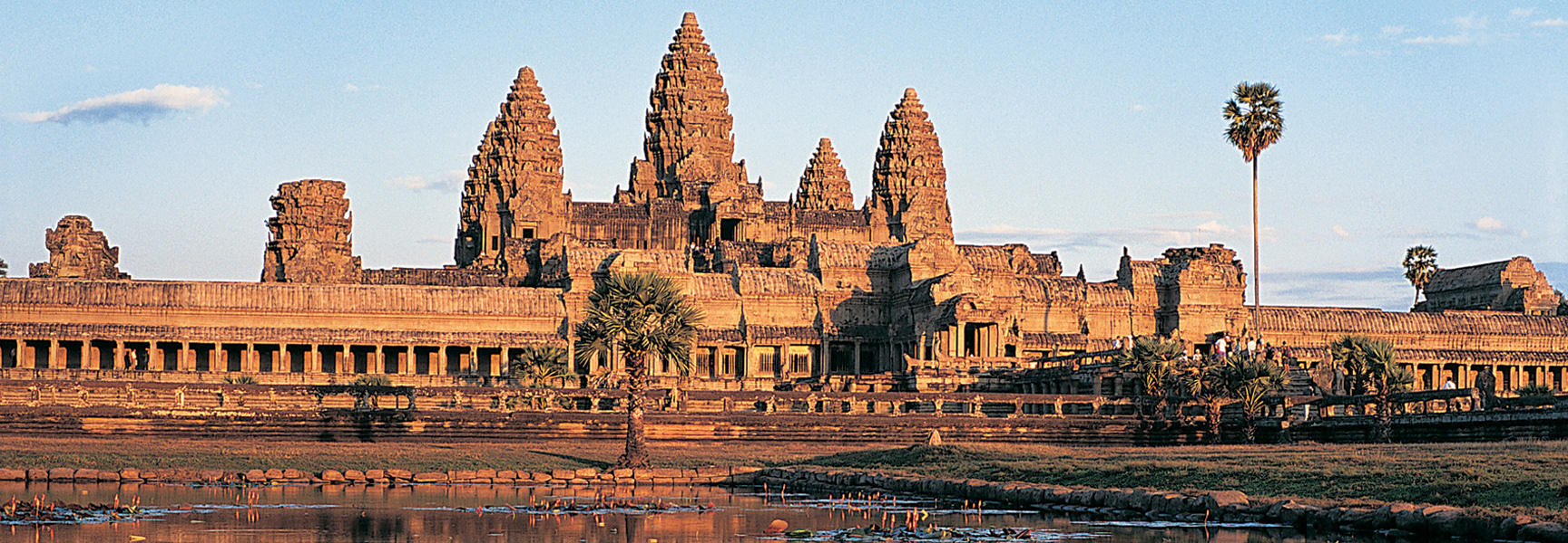 The ancient stone temple of Angkor Wat in Cambodia is bathed in golden light, its iconic towers reflected in the still waters below.
