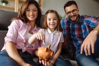 A girl pointing at a piggy bank while sitting with her family