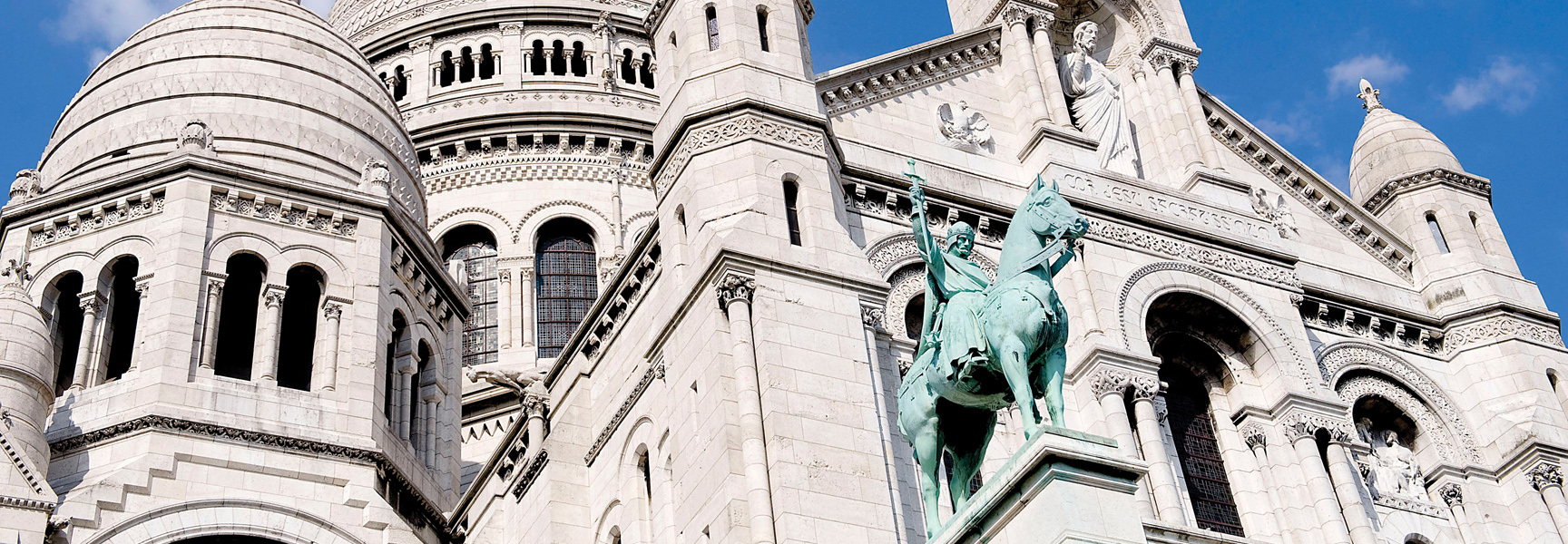 An angled, close-up view of the white-domed Sacré-Cœur Basilica in Paris, France, with a large equestrian statue in the foreground.