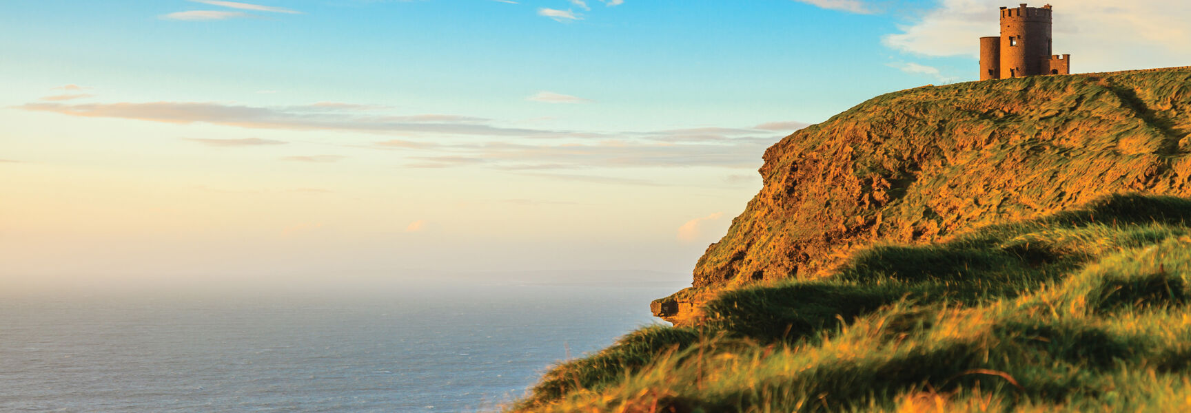 O'Brien's Tower perched on the edge of the scenic Cliffs of Moher in Ireland, overlooking the vast ocean during a golden sunset.